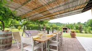 Un patio al aire libre con una mesa lista para comer, rodeado de sillas de mimbre, bajo una cubierta de bambú.