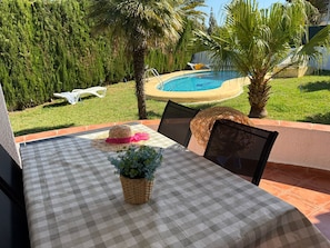 A patio with a checkered tablecloth, a wicker basket with a plant, and a straw hat.
