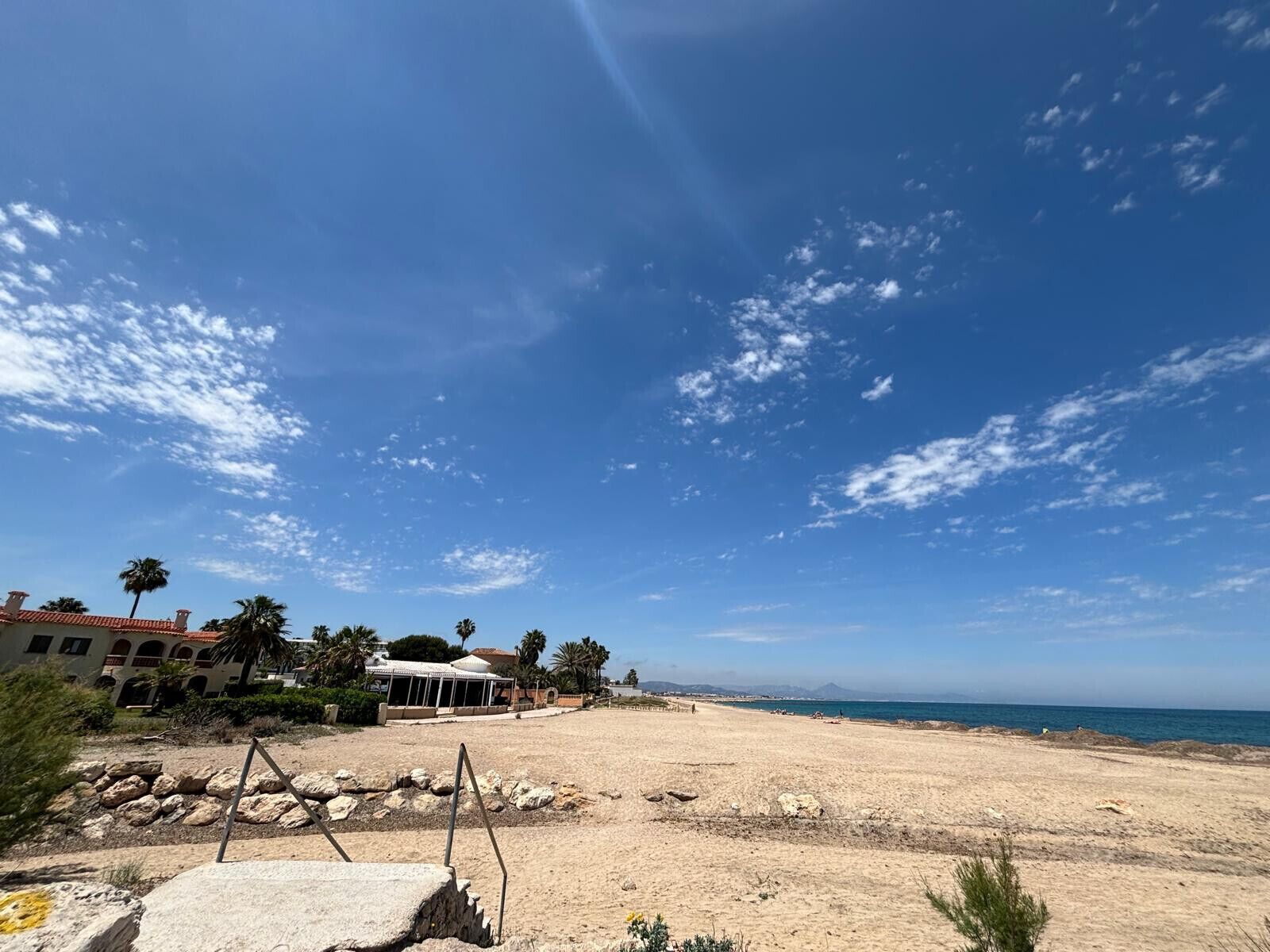 Una spiaggia con cielo sereno, alcune nuvole e un edificio con tetto rosso sullo sfondo.