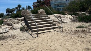 A staircase leading up to a building with multiple balconies, surrounded by sand and sparse vegetation. - 039 Villa Recuerdo (Denia)