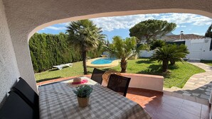 A patio with a checkered table, chairs, a potted plant, and a view of a swimming pool and greenery. - 039 Villa Recuerdo (Denia)