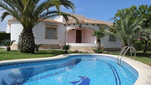 A swimming pool with a dolphin design, a house with a tiled roof, and palm trees. - 039 Villa Recuerdo (Denia)