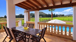 Un patio techado al aire libre con una mesa y sillas, una piscina y vistas a un paisaje verde.