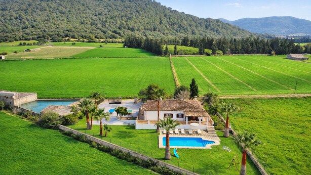 Una casa con piscina, rodeada de campos verdes y una colina arbolada.