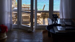 Una habitación con piso de piedra, una mesa de madera y vista al mar a través de puertas abiertas.