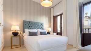 Una camera d'albergo ordinata con un letto grande, due comodini con lampade e vista attraverso una porta aperta.