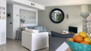 A modern living room with a white sofa, grey cushions, a round mirror, and a bowl of fruit on a wooden table. - Holiday rental semidetached with swimming pool in Begur, Sa Tuna (Begur)