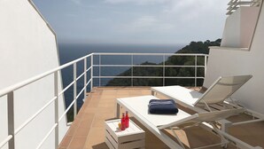 A balcony with white railings, a white table, and two lounge chairs. There are two bottles on the table. The view includes the sea and a hilly landscape. - Holiday rental semidetached with swimming pool in Begur, Sa Tuna (Begur)