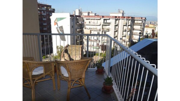 Enjoy the city view from this balcony with wicker furniture and potted plants.