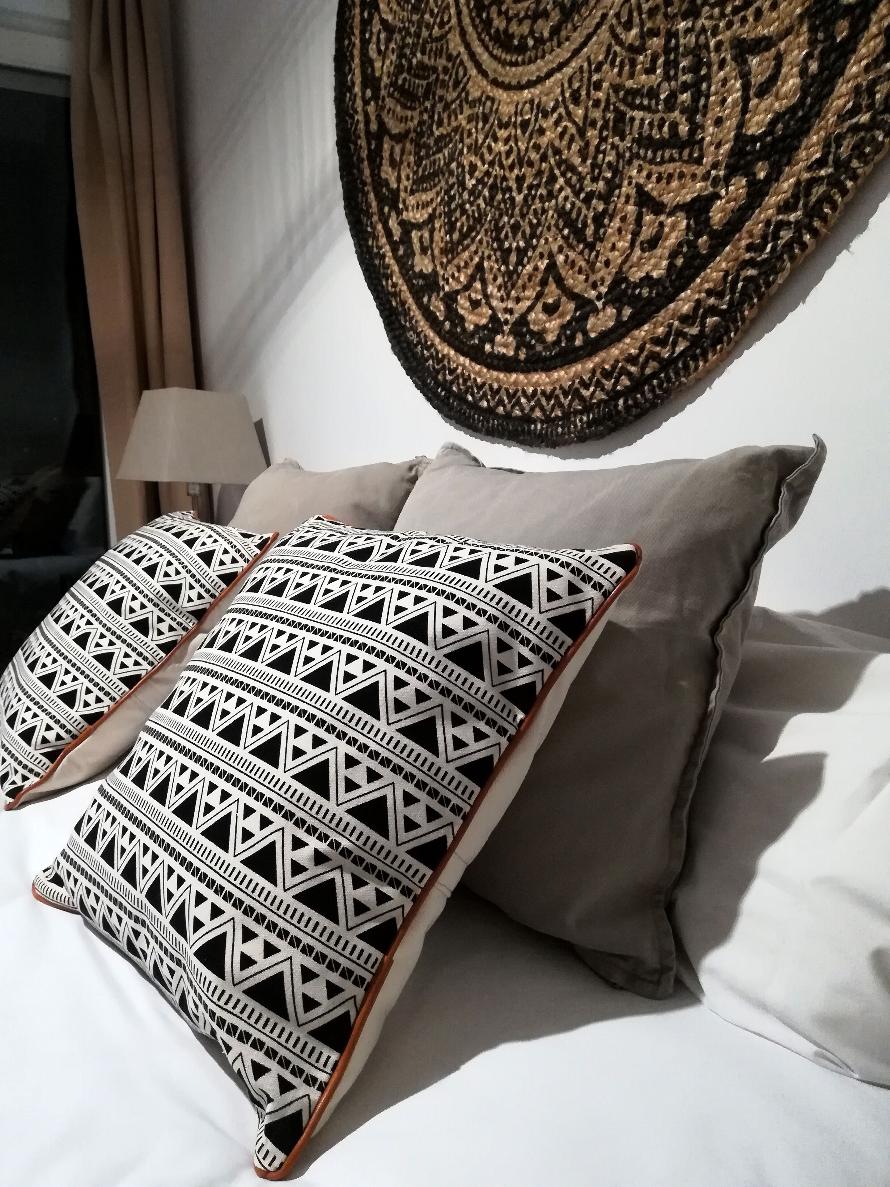Una cama con almohadones estampados, un tapiz de pared y una lámpara.