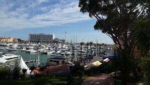 A marina with numerous boats docked, a large hotel building in the background, and a pathway leading to the marina. - Sol Nascente- Pool, Cozy, Wifi, Calm area (Vilamoura)