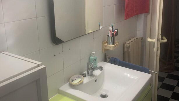 Ein Badezimmer mit einem weißen Waschbecken, einem beleuchteten Spiegel, einem roten Handtuch und einem karierten Boden.