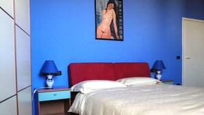 Ein Schlafzimmer mit einem roten Kopfteil, zwei Nachttischen mit Lampen, einem Bett mit weißer Bettwäsche und einer blauen Wand.