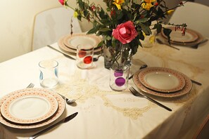 A dining table set with plates, cutlery, and a vase with flowers.