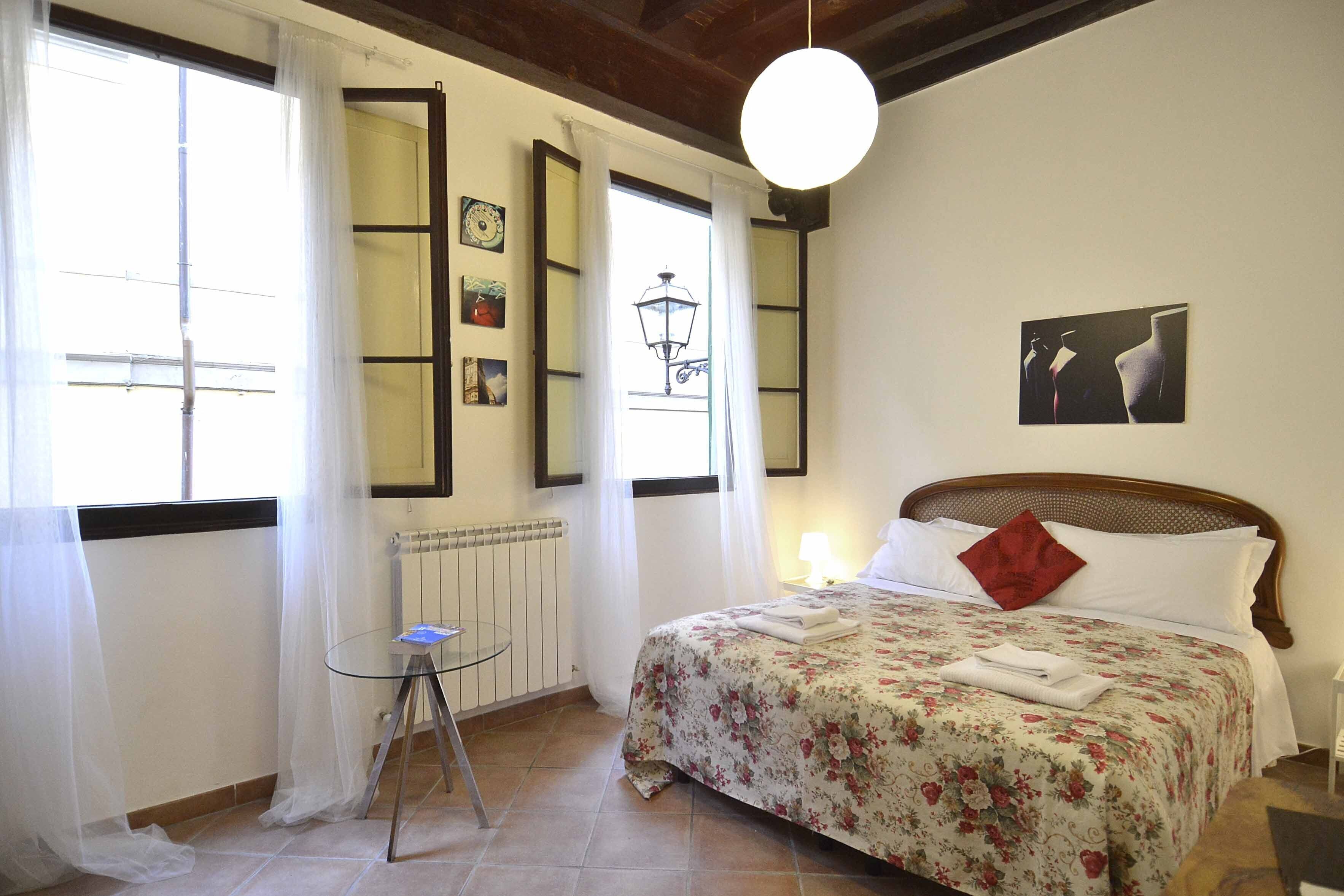 Ein Schlafzimmer mit Bett, einem kleinen Tisch und einem Fenster mit Vorhängen.