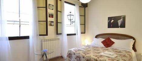 Un dormitorio con una cama, una mesita y una ventana con cortinas.