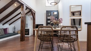 Un comedor con mesa de madera, sillas de mimbre, chimenea y escalera con vigas a la vista.