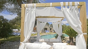 A wooden canopy bed with white linens and curtains, overlooking a pool and a stone building. - Moli - Rural house with pool in Búger (Buger)