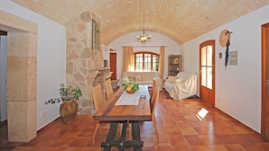 A dining area with a wooden table, chairs, a vase with flowers, and a stone wall. - Moli - Rural house with pool in Búger (Buger)
