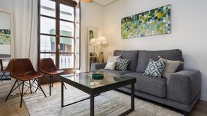 A modern living room with a grey sofa, two brown chairs, a glass coffee table, and a colorful abstract painting on the wall. - Genteel Home Mateos Gago III (Seville)