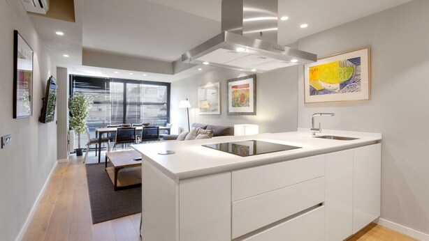 Una cocina moderna con una isla central, armarios blancos y una campana extractora de acero inoxidable.