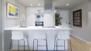 Una cocina moderna con una isla central, electrodomésticos de acero inoxidable y taburetes blancos.