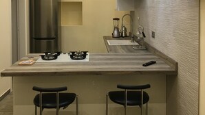 Une cuisine compacte dotée d’un réfrigérateur encastré, d’une cuisinière à gaz, de deux tabourets de bar et d’un luminaire suspendu moderne.