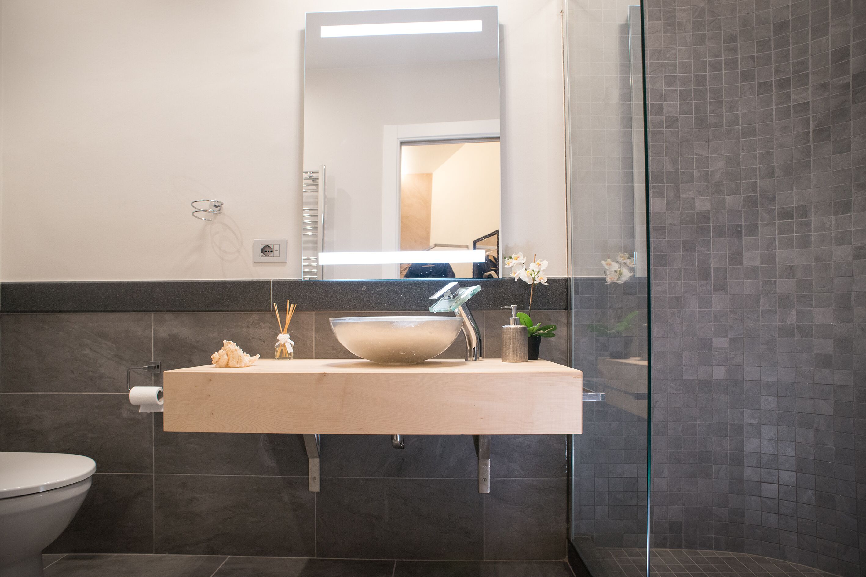 A bathroom with a modern sink, mirror, and dark tiled walls.