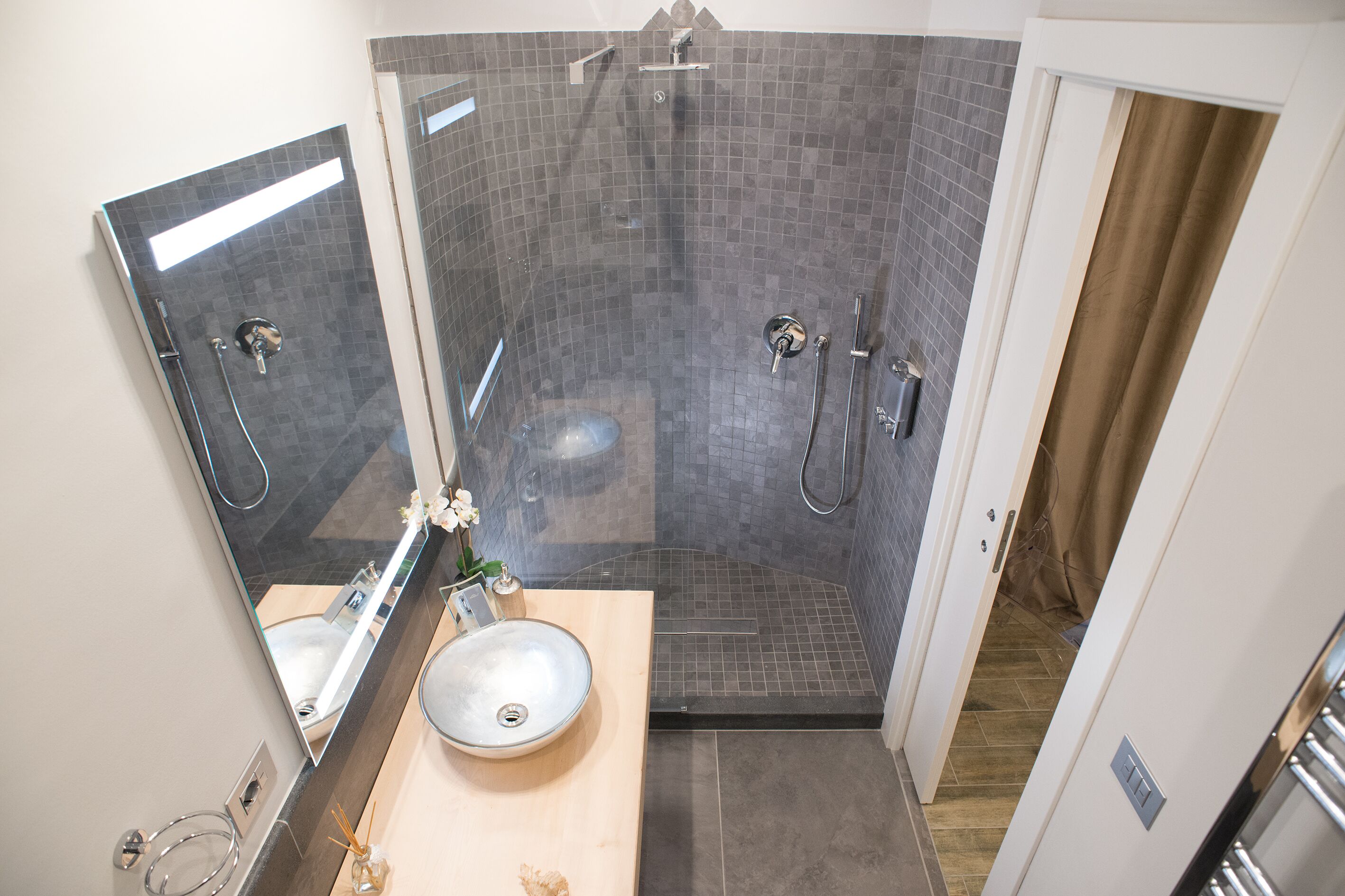 Une salle de bain moderne dotée d’une douche à parois de verre, d’un lavabo avec un receveur et d’un miroir au-dessus du meuble-lavabo.
