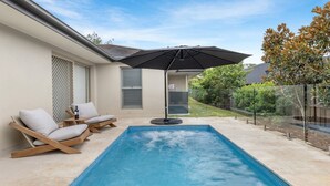 Ein Schwimmbecken mit zwei Liegestühlen und einem Tisch, einer überdachten Whirlpool-Anlage und einer überdachten Terrasse.