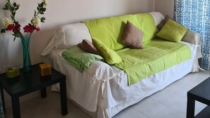 A modern living room with a green sofa, white cushions, and two pink floral wall art pieces.