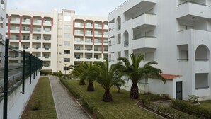 A modern multi-story building with balconies, a paved walkway, and palm trees.