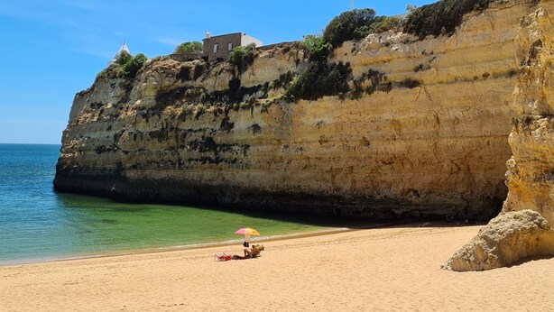 A beach with a rocky cliff, a lighthouse, and a sandy shore.