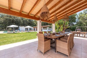 Une terrasse extérieure aménagée avec des meubles en osier, un plafond en bois et une vue sur une piscine et un jardin.