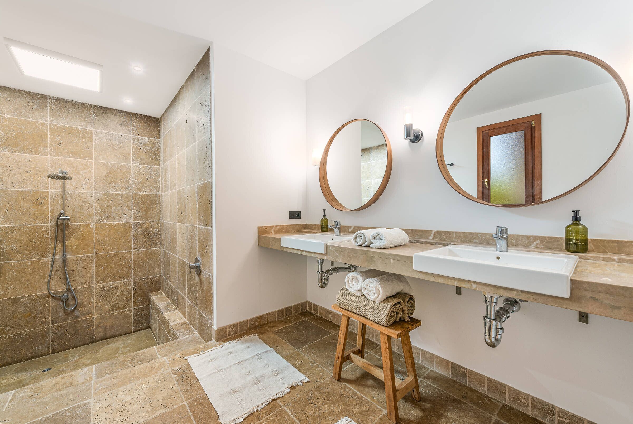 Un baño con dos lavamanos, una ducha y un taburete de madera.