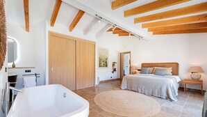Ein modernes Schlafzimmer mit einer großen Badewanne, einem Bett mit Kissen, einem Nachttisch mit Lampe und einer Holzzahl.