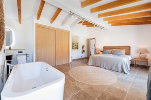 Une chambre à coucher moderne avec une grande baignoire, un lit avec des oreillers, une table de chevet avec une lampe et un plafond en bois.
