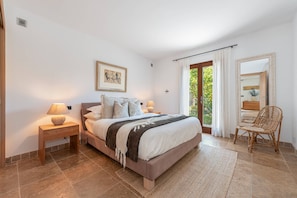A bedroom with a bed, nightstands, a chair, a window with curtains, and a framed picture on the wall.