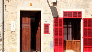 Ein Gebäude aus Stein mit einer Holztür und roten Fensterläden.