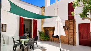 Eine Terrasse mit Tisch und Stühlen, einem weißen Sonnenschirm und roten Fensterläden an einem Gebäude.