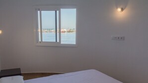 Ett rum med en säng, ett fönster med utsikt över en småbåtshamn och ett eluttag.