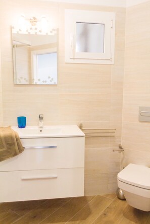 Une salle de bain avec un lavabo blanc, un miroir, une serviette, des toilettes et un espace douche.