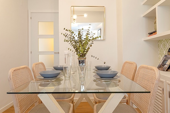 A dining area with a glass table, wicker chairs, and a vase with green foliage.