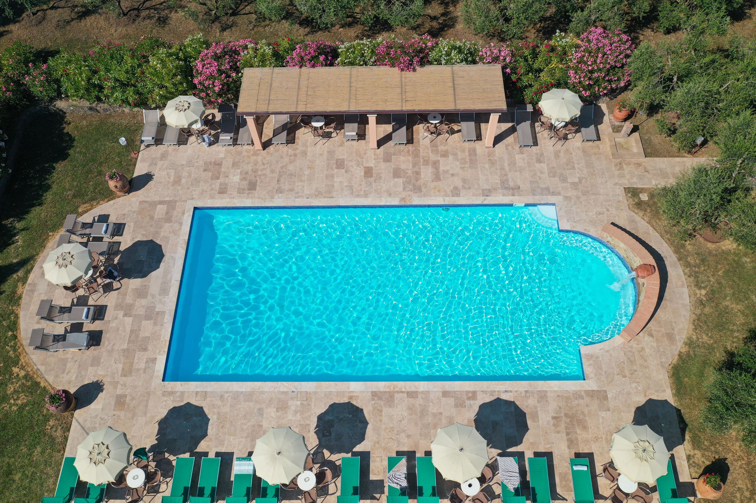 A rectangular swimming pool with a curved edge, surrounded by lounge chairs and umbrellas.