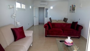Ein Wohnzimmer mit einem beigen Sofa, einem roten Samtsofa, einem Glastisch und einer Vase mit einer Kerze.