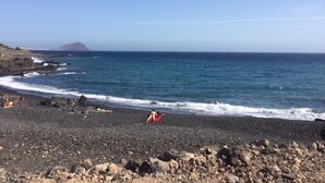 A rocky beach with waves crashing onto the shore, a clear sky, and a distant mountain.
