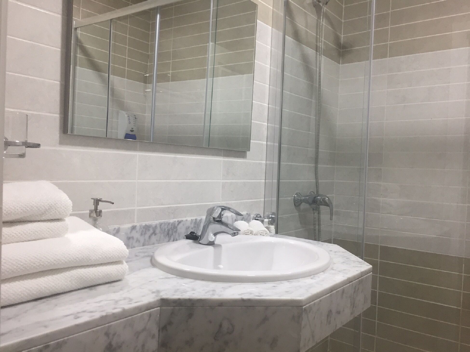 Un baño con lavamanos de mármol, cabina de ducha de vidrio y un espejo grande.