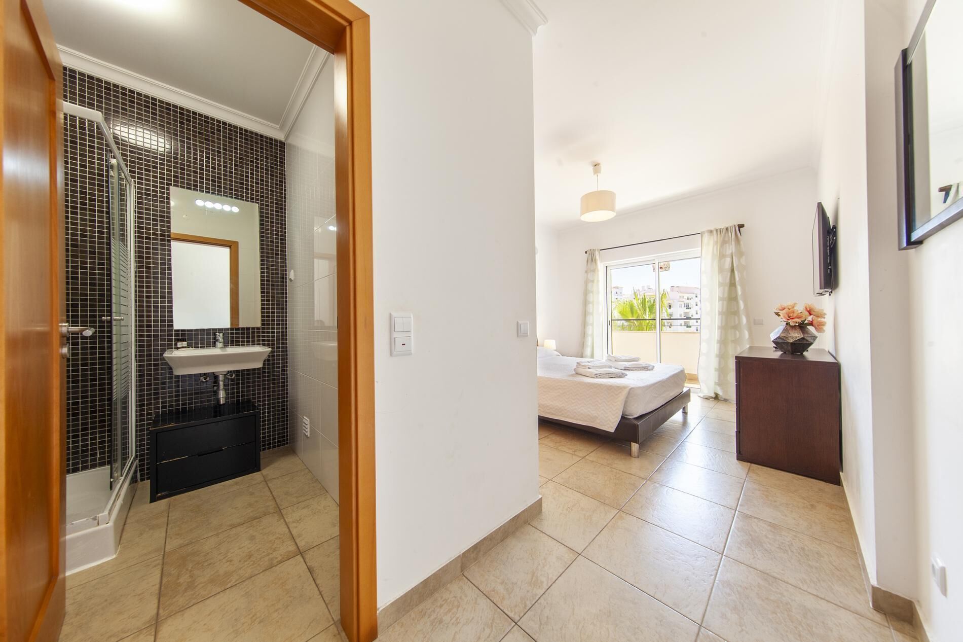 A hotel room with a bathroom, a bed, a bedside table, and a view of the outside.