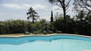 A swimming pool with a curved edge, surrounded by green lounge chairs and a stone deck.