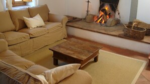 A cozy living room with a sofa, a coffee table, and a fireplace with logs.